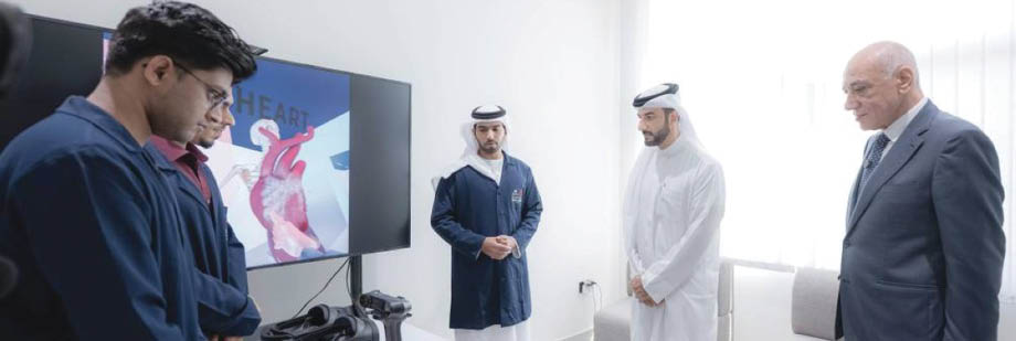 مجموعة من الأشخاص يرتدون ملابس تقليدية ورسمية يقفون في غرفة بجانب شاشة تعرض رسمًا توضيحيًا لقلب بشري. Description generated by AI