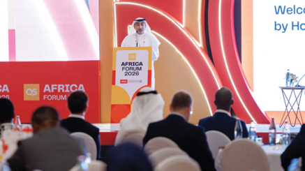 شخص يرتدي زيًا تقليديًا يتحدث من منصة في مؤتمر أفريقيا 2026 أمام جمهور جالس في قاعة مؤتمرات مزينة بألوان دافئة. Description generated by AI