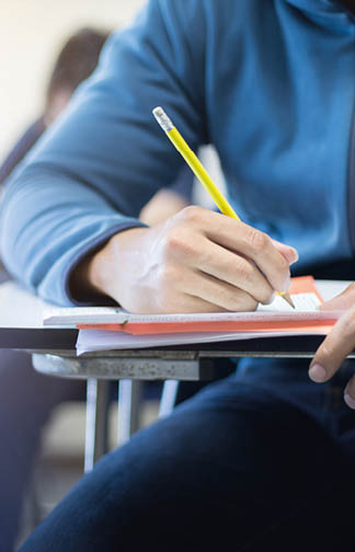 soft focus.high school or university student holding pencil writing on paper answer sheet.sitting on lecture chair taking final exam attending in examination room or classroom.student in uniform.