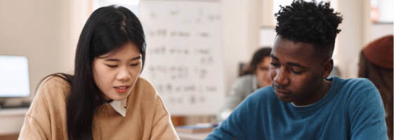 Front view portrait of two multiethnic students Asian woman and Black man studying together sitting at table in college library