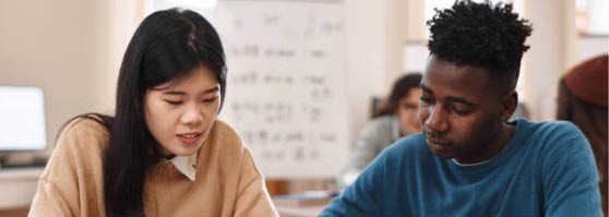 Front view portrait of two multiethnic students Asian woman and Black man studying together sitting at table in college library
