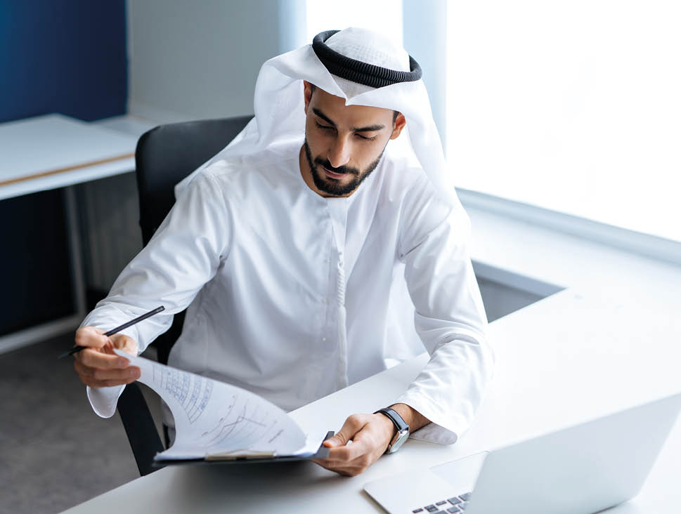 Handsome man with dish dasha working in his business office of Dubai. Portraits of a successful businessman in traditional emirates white dress. Concept about middle eastern cultures.